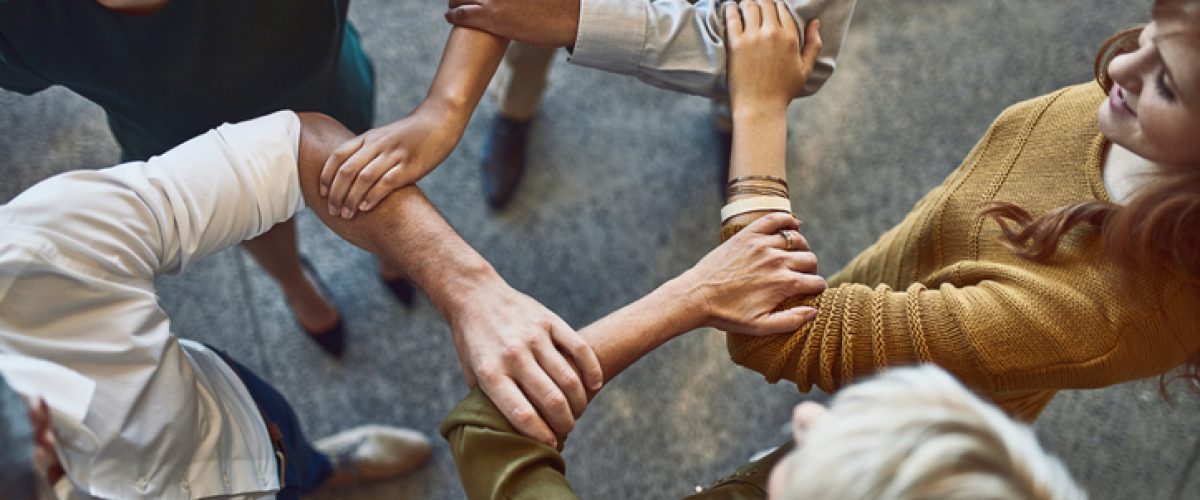 High angle shot of a group of colleagues linking arms in solidarity at work